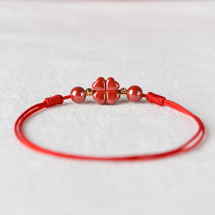 Rotes Armband Zinnober Kleeblatt mit goldenen Perlen auf weißem Hintergrund Nahaufnahme