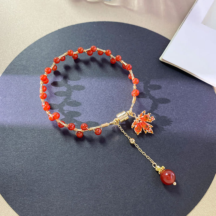 Rotes Armband mit Ahornblatt-Charm und Glücksperlen elegant präsentiert.