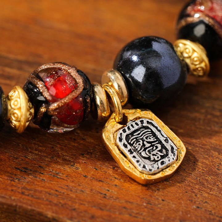Armband Zakiram – Glück & Wohlstand mit roten und schwarzen Steinen golden verziert.