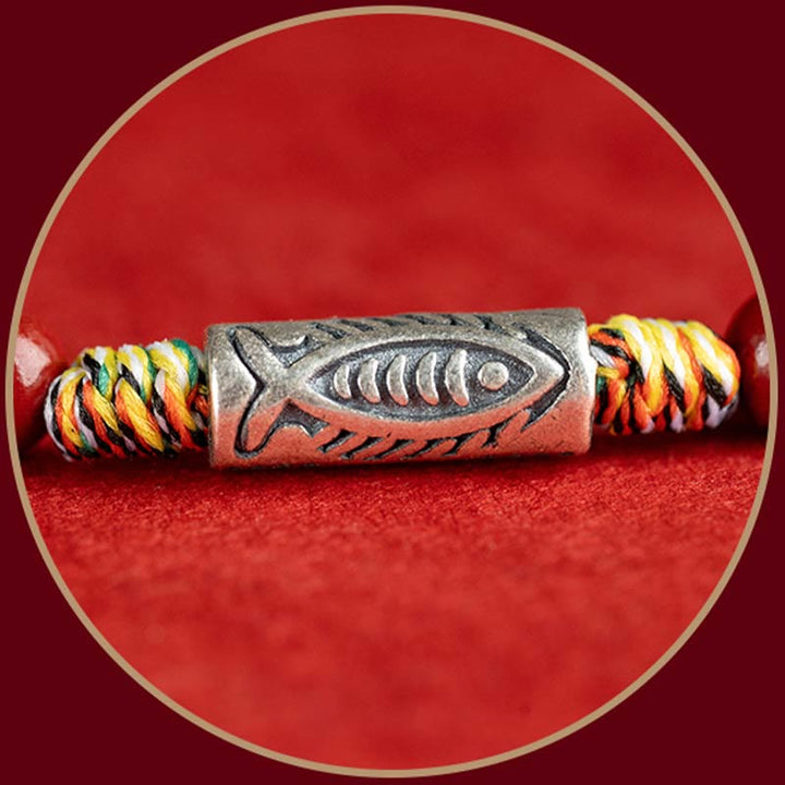 Armband mit Koi Fisch Anhänger und bunten Seilen auf rotem Hintergrund.