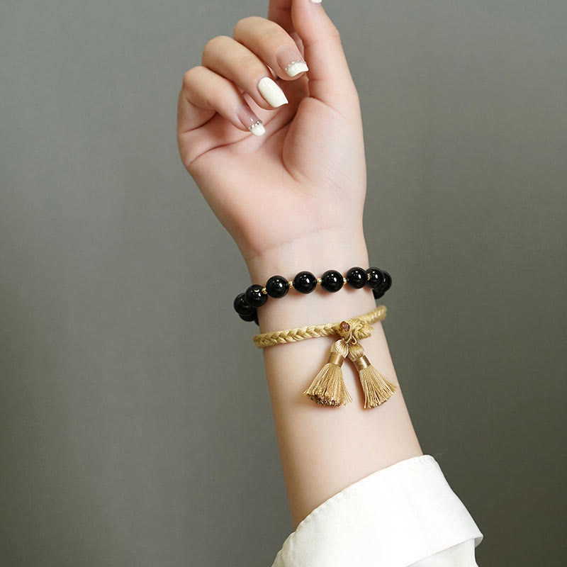 Armband Schwarzer Onyx – Schutz mit goldenen Quasten elegant getragen.