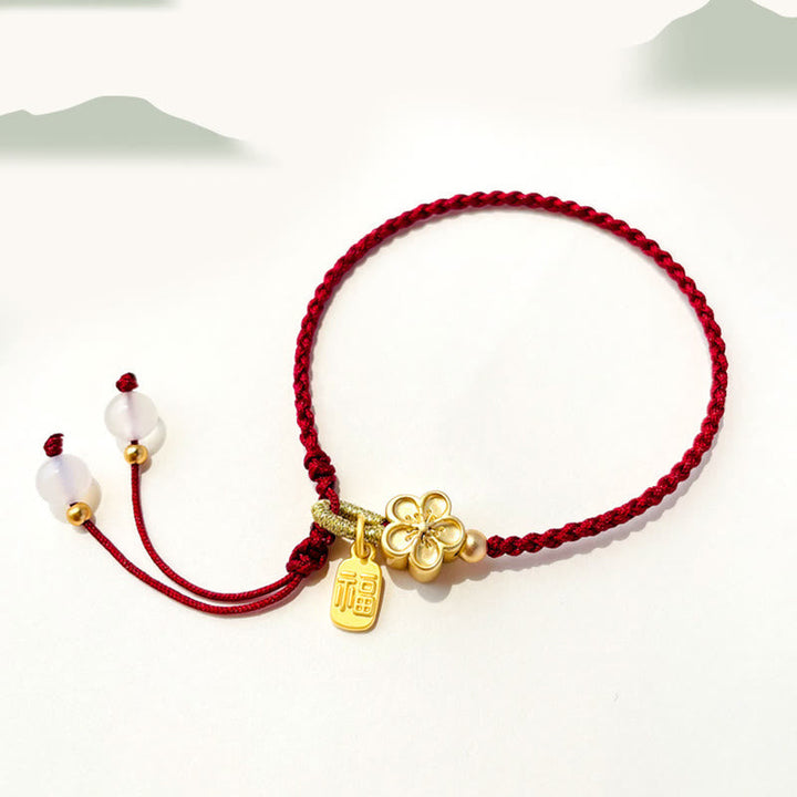 Rotes Armband Pfirsichblüte mit goldenem Anhänger und weißen Perlen.