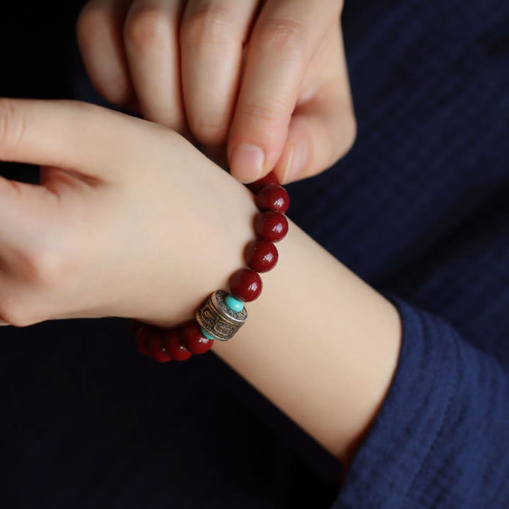 Rotes Perlenarmband mit silbernem Om Mani Padme Hum Anhänger am Handgelenk.