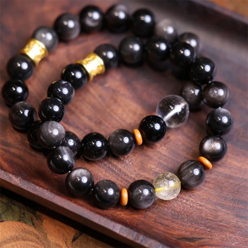 Schwarzes Obsidian Armband mit goldenen Perlen auf Holzplatte arrangiert.