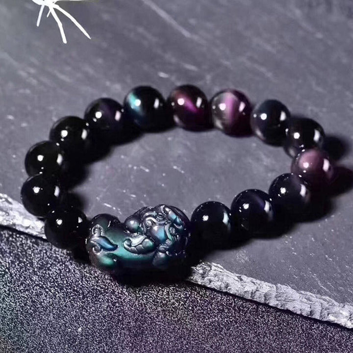 Schwarzes Obsidian Pixiu Armband mit Regenbogenglanz auf grauem Untergrund