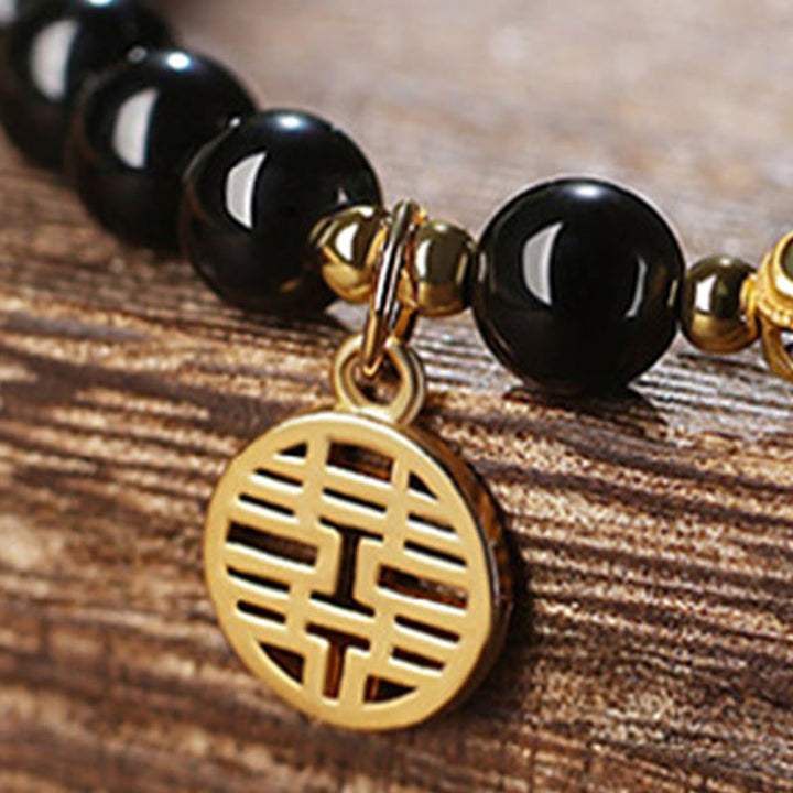 Armband Schwarzer Obsidian Jade mit goldenem Anhänger auf Holz
