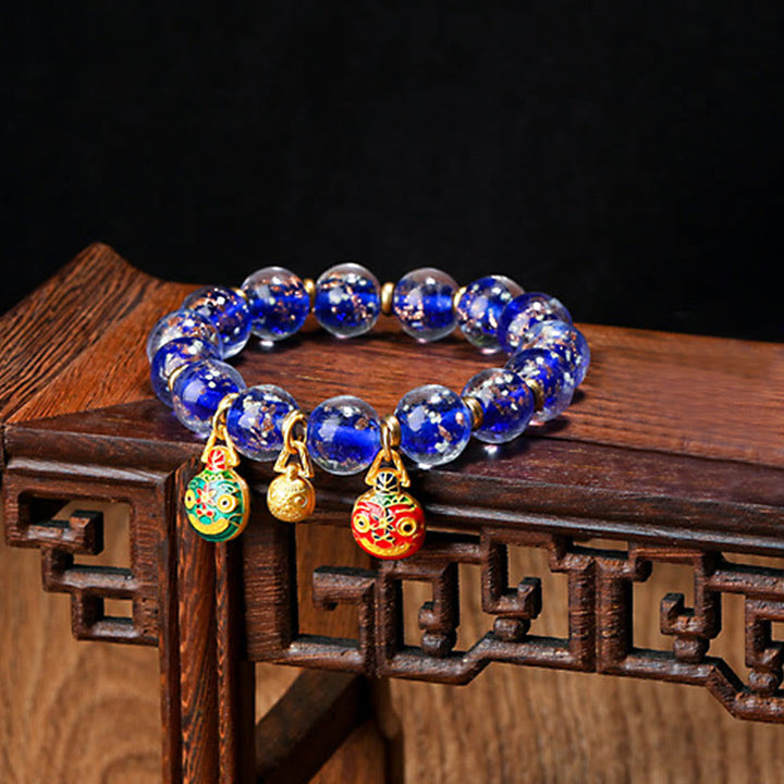 Blaues Perlenarmband mit goldenen Anhängern auf Holzoberfläche.