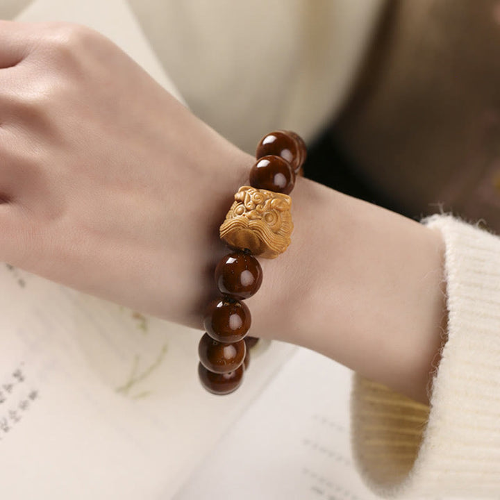 Armband mit braunen Perlen und goldenem Löwen Anhänger.