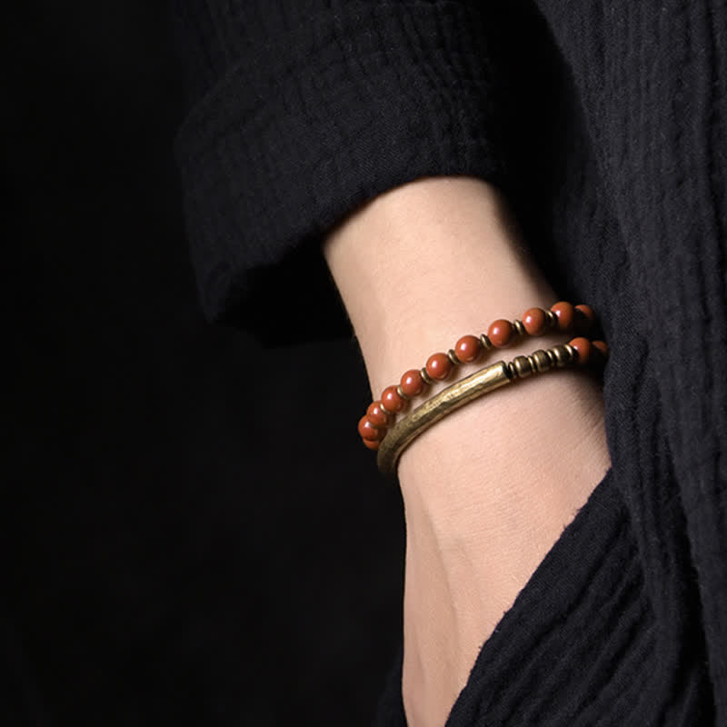 Zwei elastische Armbänder mit roten Perlen und Metallakzenten am Handgelenk getragen.