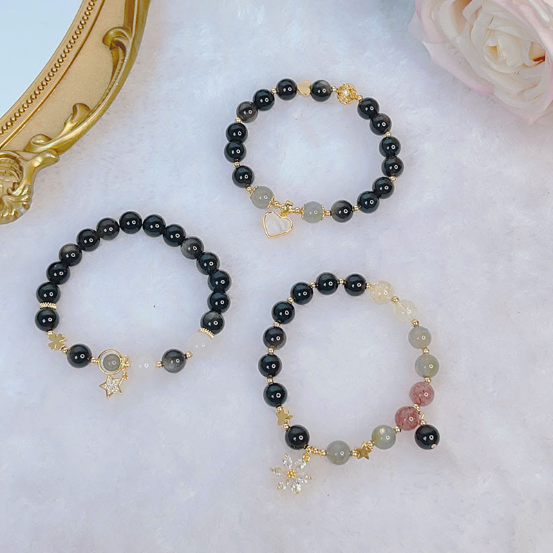 Drei Obsidian Armbänder mit goldenen Charms auf weißem Hintergrund.