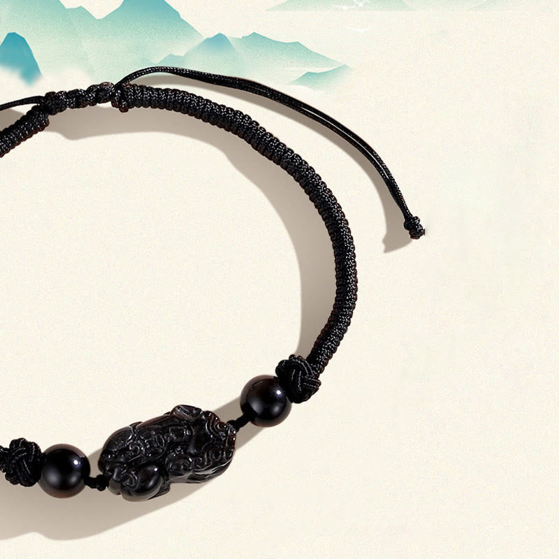 Schwarzes Obsidian Pixiu Armband mit Perle auf beiger Oberfläche.