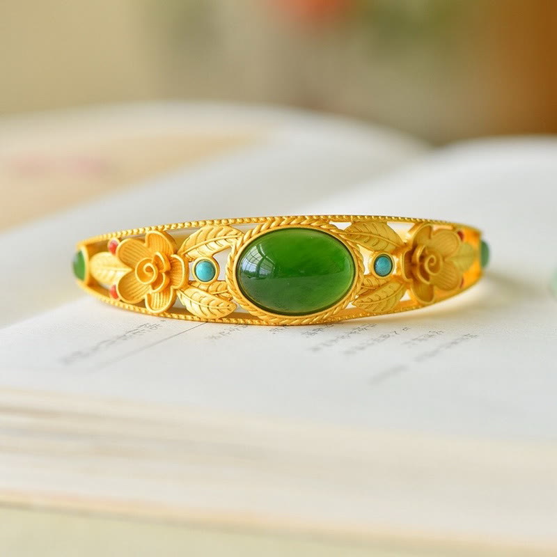Goldenes Armband mit grüner Jade und Blütendesign auf Marmor.