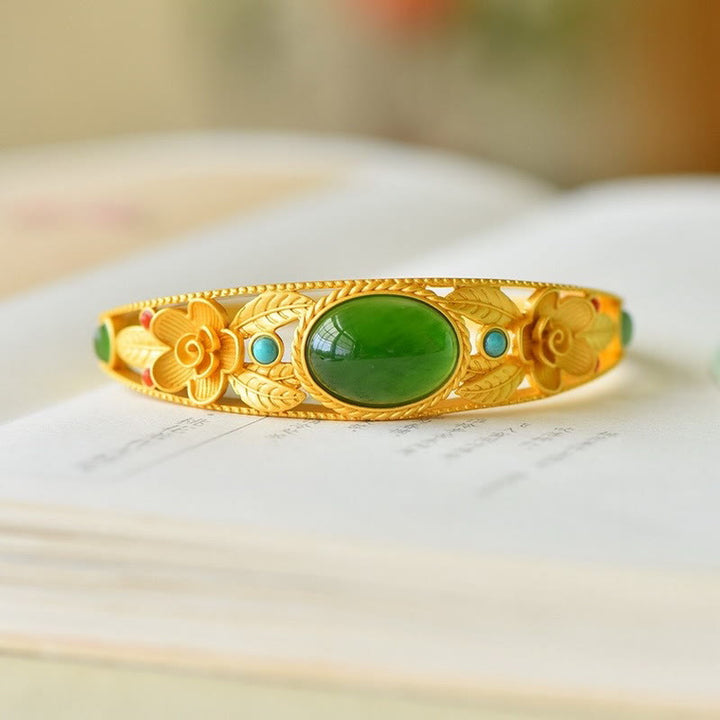 Goldenes Armband mit grüner Jade und Blütendesign auf Marmor.