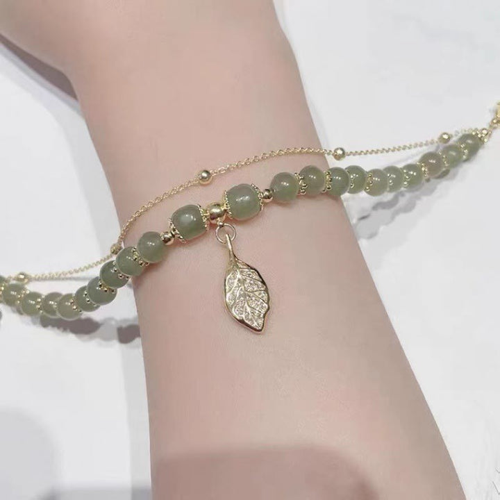 Jade Armband mit Blattanhänger am Handgelenk, goldene Kettenglieder elegant.