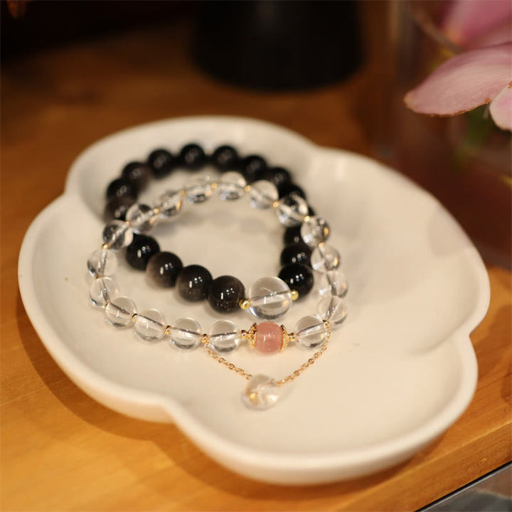 Drei Armbänder mit Obsidian, Kristall und rosé Perlen auf weißer Schale.