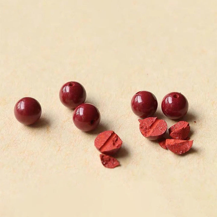 Rote Granatapfelkerne und ganze Früchte auf beiger Fläche, Armband Zinnober – Glück & Segen.