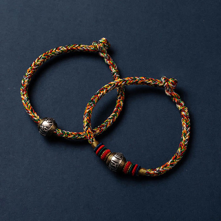 Zwei geflochtene bunte Armbänder mit silbernen Perlen auf grauem Hintergrund.