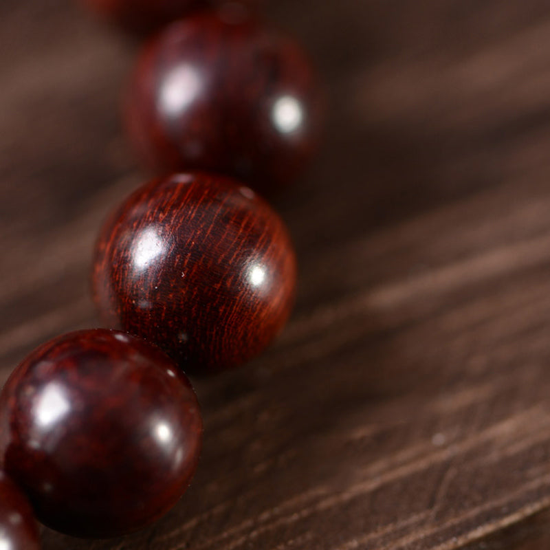 Rote Sandelholz Perlen Armband mit glänzender Oberfläche auf Holzhintergrund.