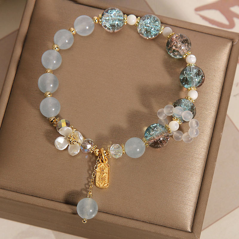 Elegantes Armband mit Mondstein und glitzernden Kristallperlen auf beiger Oberfläche.