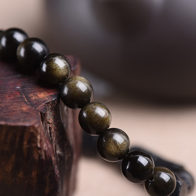 Obsidian Armband Wohlstand goldglänzend Perlen Holzoberfläche Nahaufnahme Naturstein