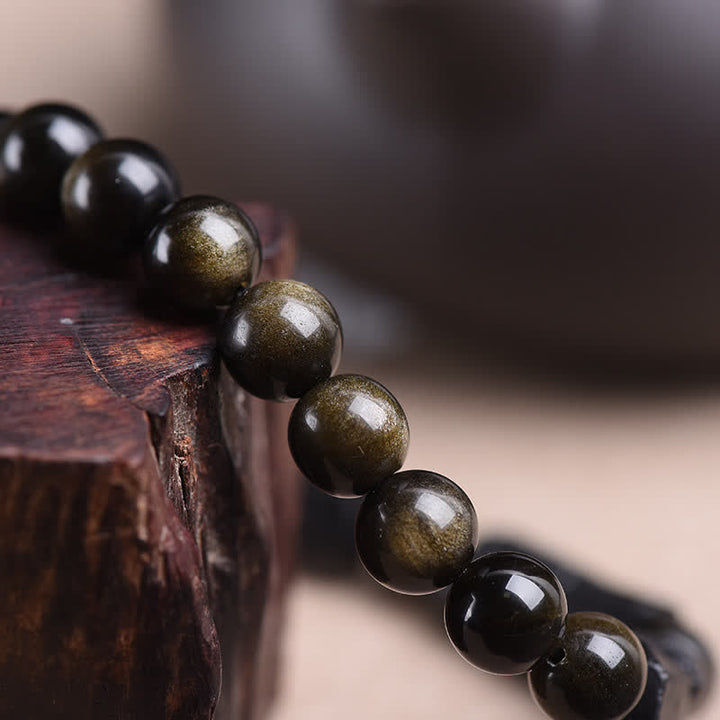 Obsidian Armband Wohlstand goldglänzend Perlen Holzoberfläche Nahaufnahme Naturstein