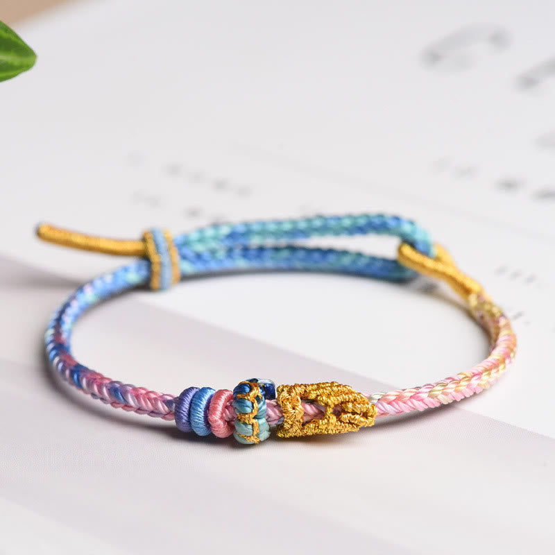 Buntes geflochtenes Armband mit Friedensknoten und goldenem Verschluss auf weißem Hintergrund.