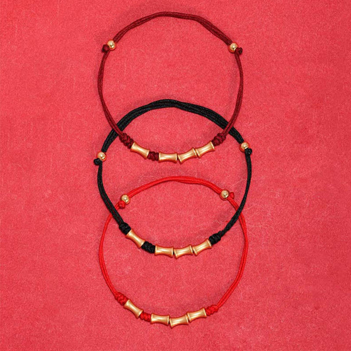 Drei bunte Armbänder mit Bambus-Perlen aus Gold auf rotem Hintergrund.