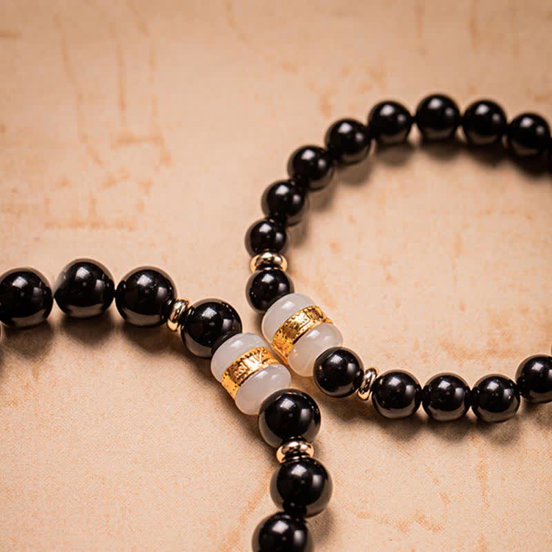 Schwarzes Obsidian Armband mit goldenen Perlen auf beiger Oberfläche.