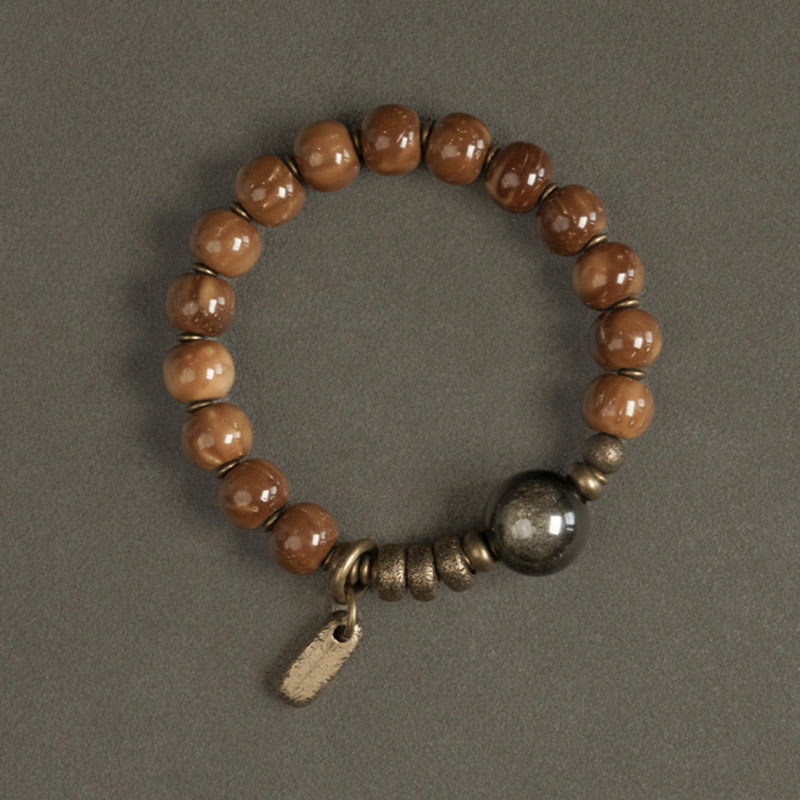 Armband mit braunen Perlen und silbernem Anhänger auf grauem Untergrund.