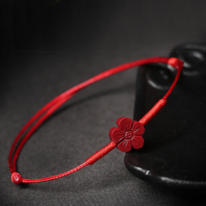 Rotes Seidenarmband mit Blütenanhänger auf dunklem Hintergrund, Nahaufnahme.