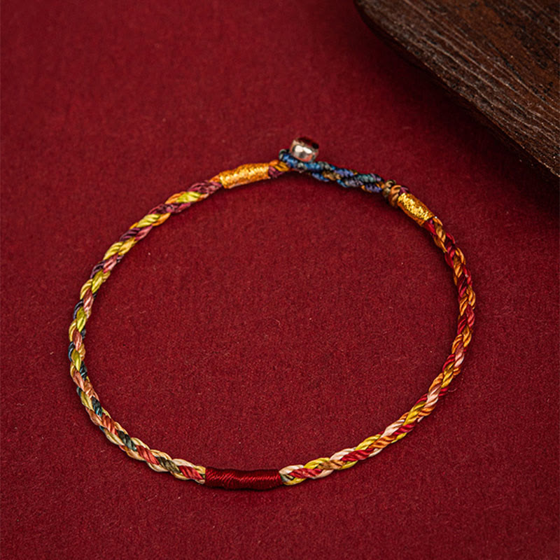 Fünffarben geflochtenes Armband mit goldenem Faden auf rotem Untergrund Flat-lay