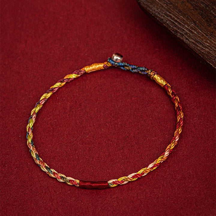 Fünffarben geflochtenes Armband mit goldenem Faden auf rotem Untergrund Flat-lay