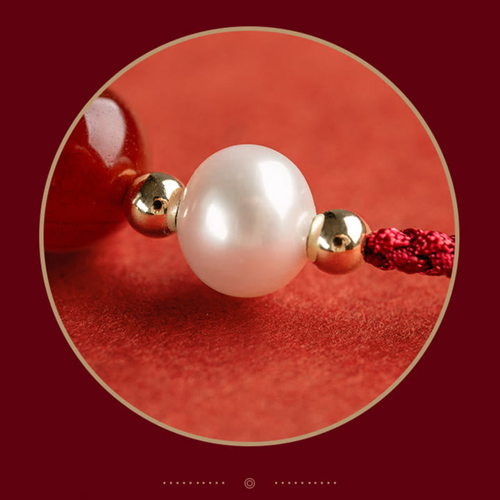 Elegantes Armband mit Perle und goldenen Kugeln auf rotem Hintergrund.