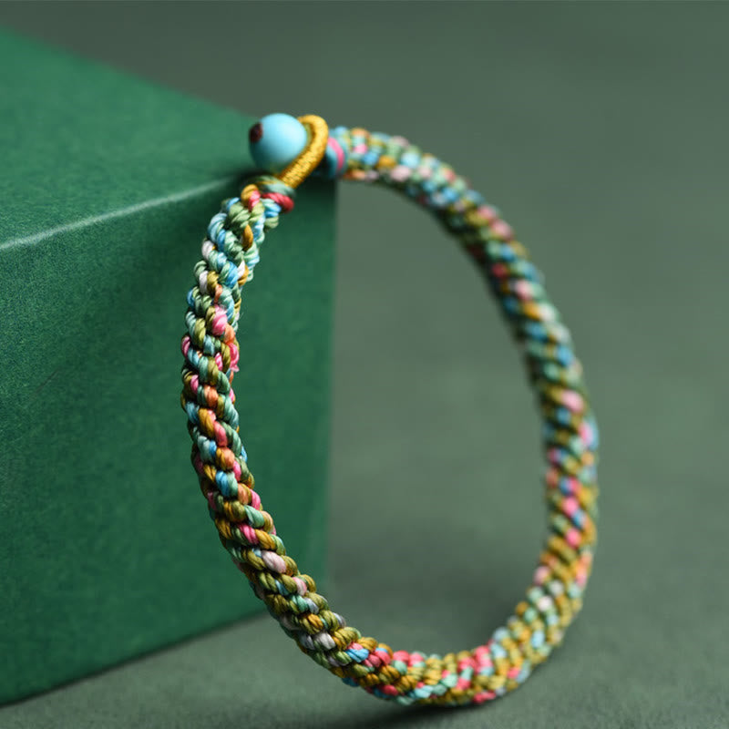Buntes geflochtenes Armband mit Glücksperle auf grünem Hintergrund
