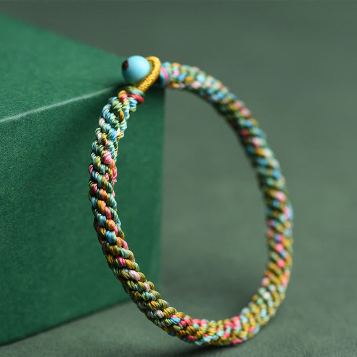 Buntes geflochtenes Armband mit Glücksperle auf grünem Hintergrund