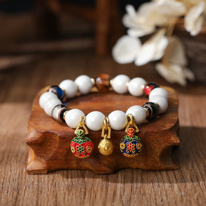 Weißes Perlen Armband mit bunten Emaile Anhängern auf Holz.