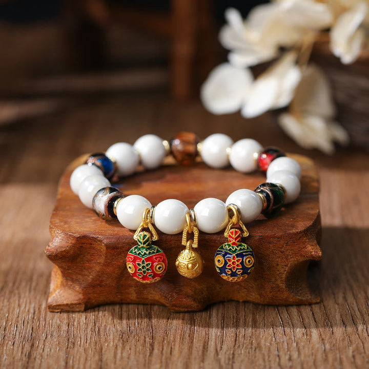 Weißes Perlen Armband mit bunten Emaile Anhängern auf Holz.