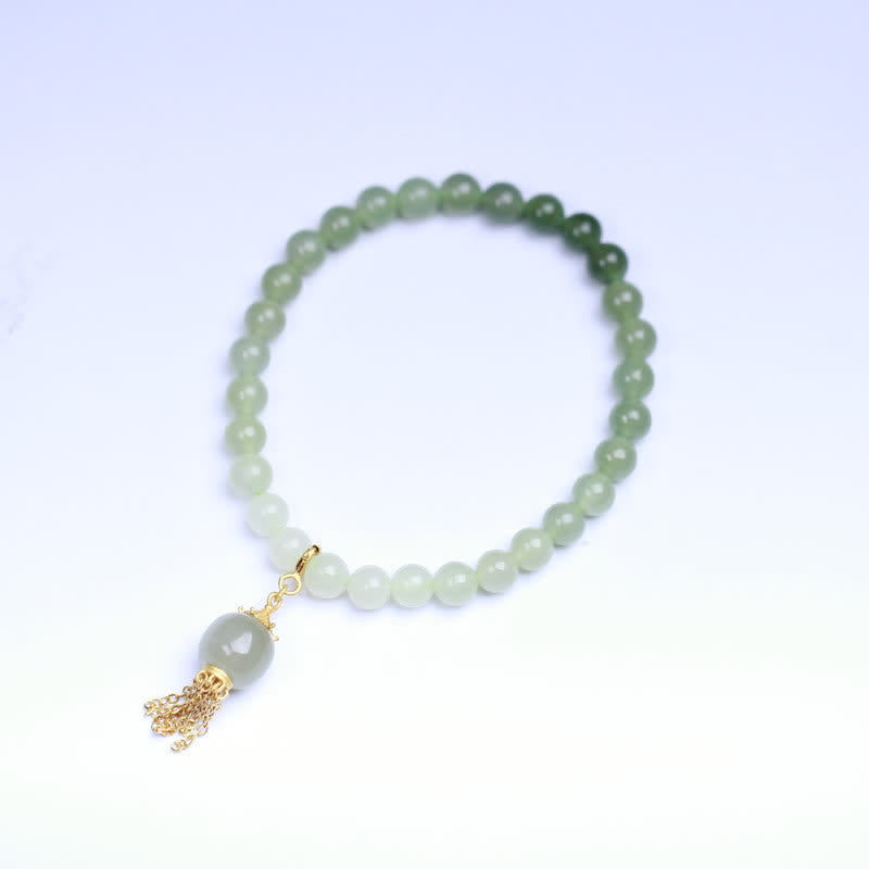 Jadegrünes Perlenarmband mit goldenem Quastenanhänger auf hellblauem Hintergrund