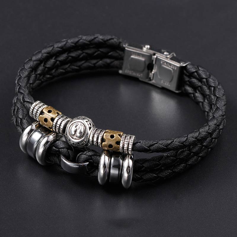 Schwarzes Leder-Armband mit Hämatit und Metallverzierungen auf grauem Hintergrund.
