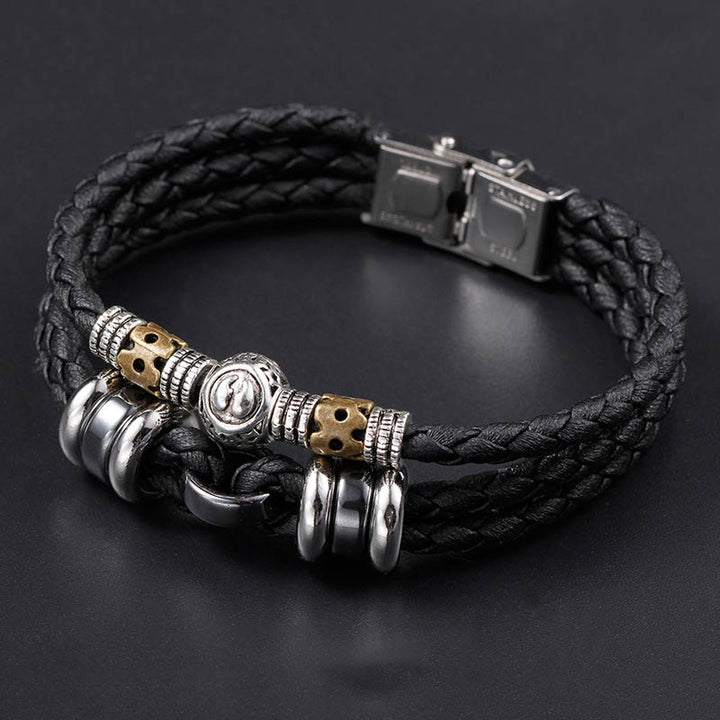 Schwarzes Leder-Armband mit Hämatit und Metallverzierungen auf grauem Hintergrund.