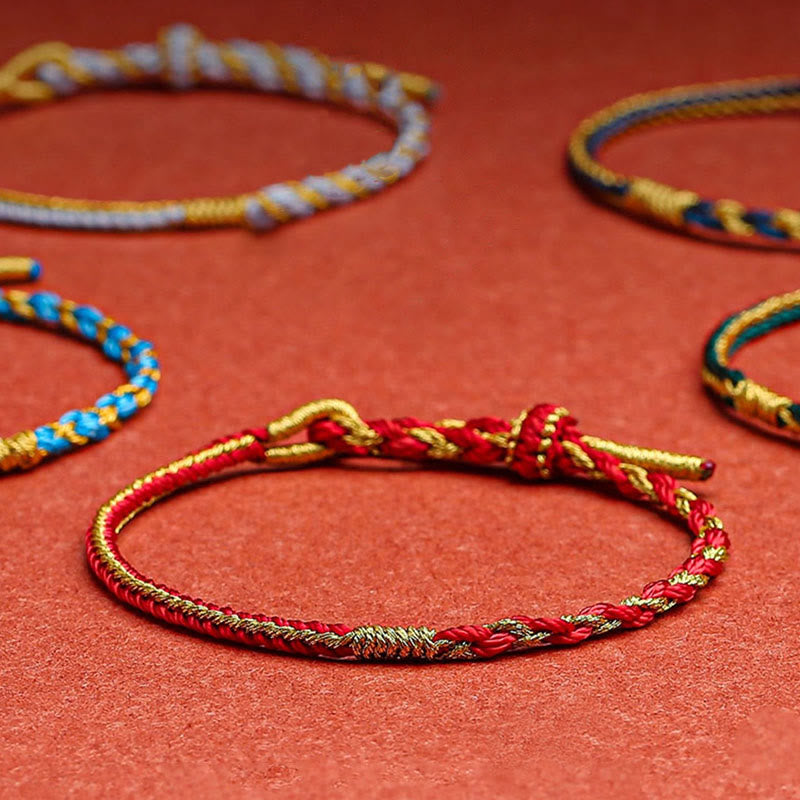 Rote und goldene geflochtene Armbänder auf rotem Hintergrund angeordnet.