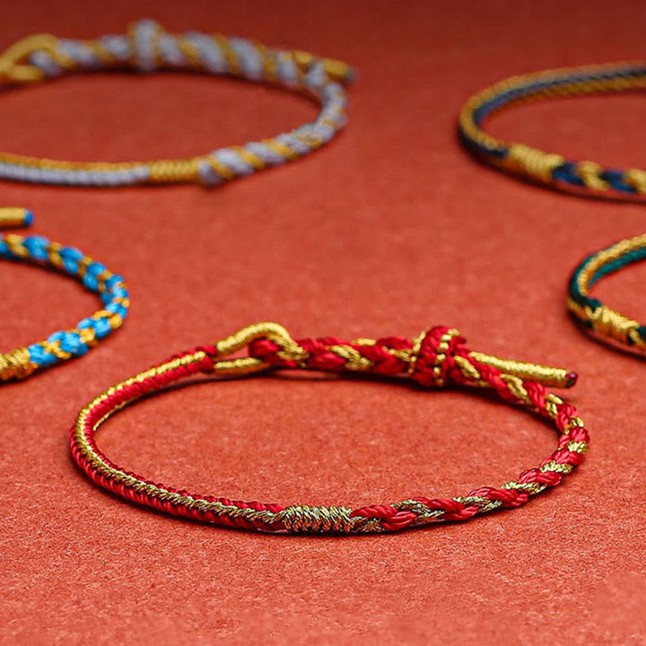 Rote und goldene geflochtene Armbänder auf rotem Hintergrund angeordnet.