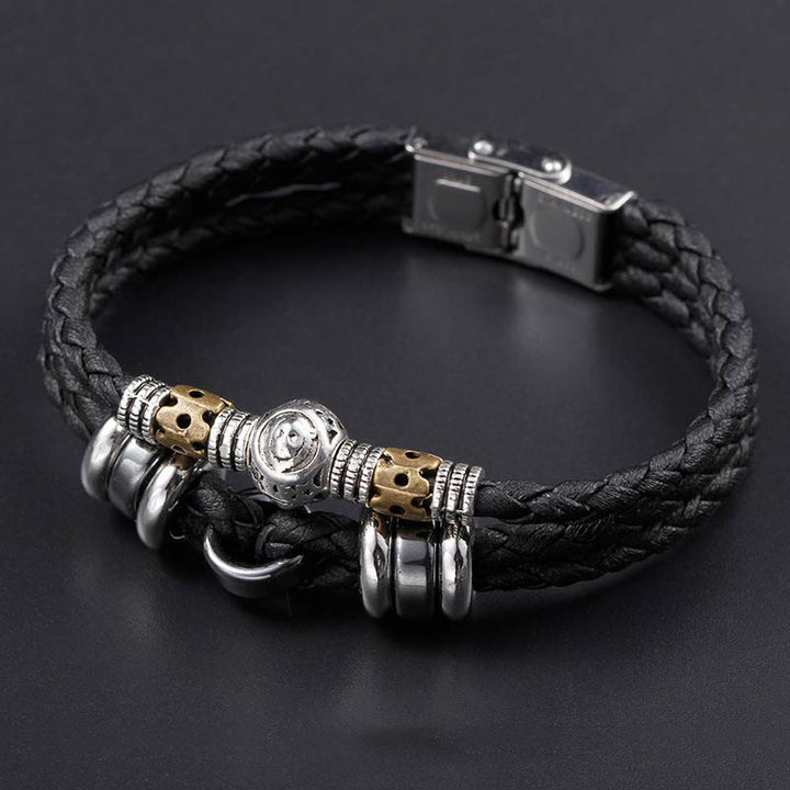 Schwarzes Lederarmband mit Hämatit Tierkreiszeichen Charm auf grauem Hintergrund.
