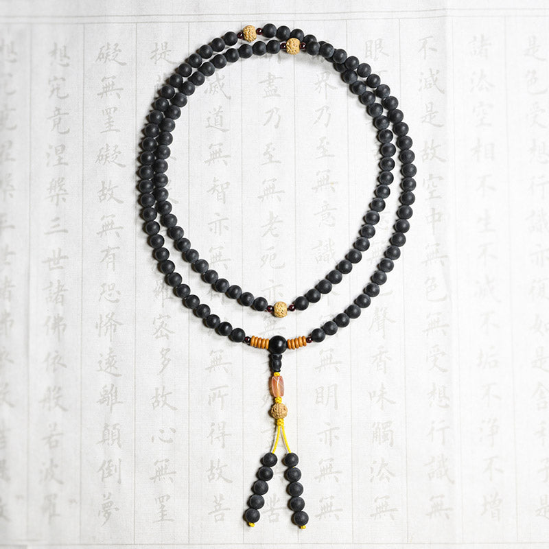 Schwarze Mala-Kette mit Bodhi-Perlen auf strukturiertem Hintergrund flach.