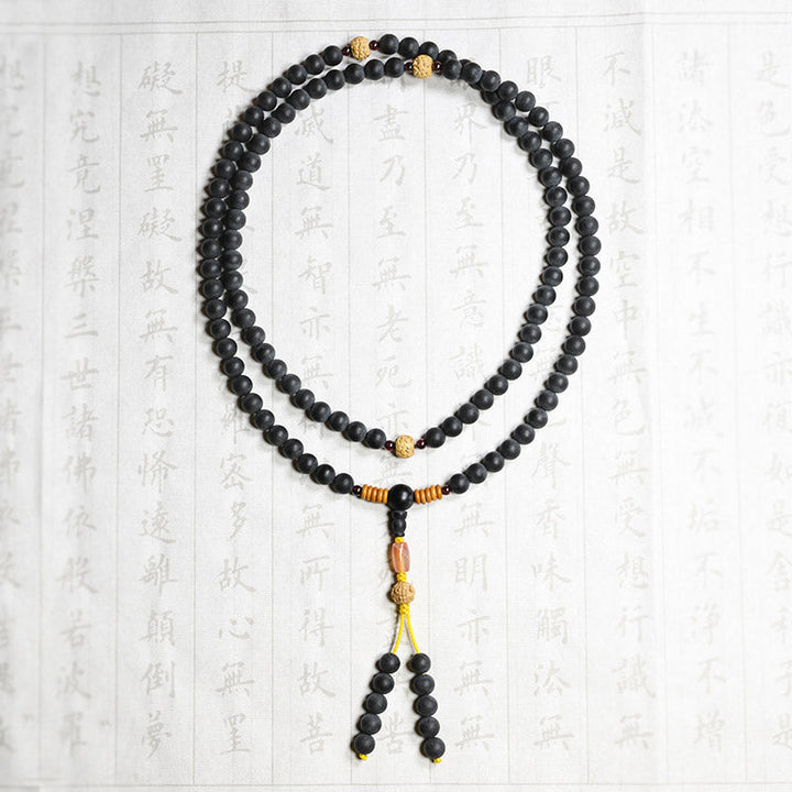 Schwarze Mala-Kette mit Bodhi-Perlen auf strukturiertem Hintergrund flach.