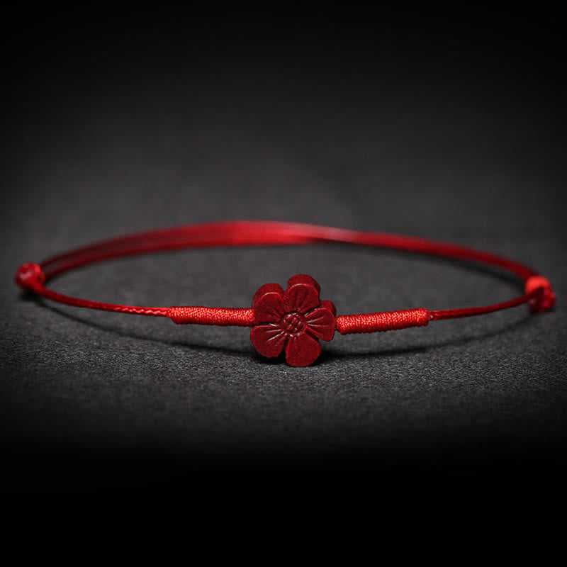 Rotes Armband mit Blüten-Anhänger auf dunklem Hintergrund, Nahaufnahme.