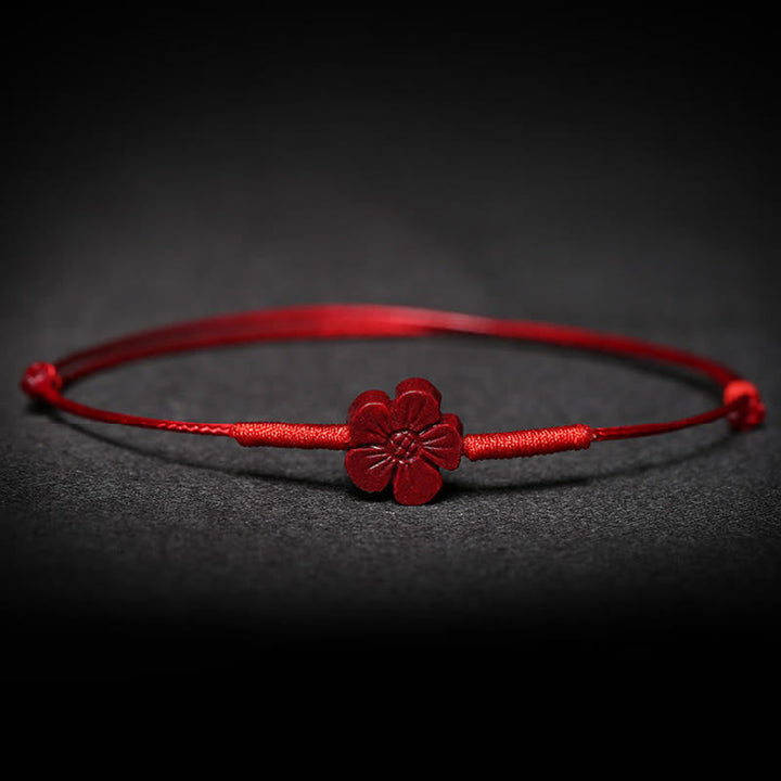Rotes Armband mit Blüten-Anhänger auf dunklem Hintergrund, Nahaufnahme.