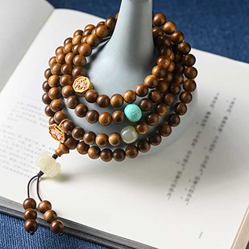 Mala Rosenholz Armband mit farbigen Steinen auf offenem Buch.