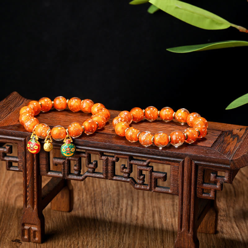 Orangefarbenes Perlenarmband auf Holzständer mit Jade-Anhängern.