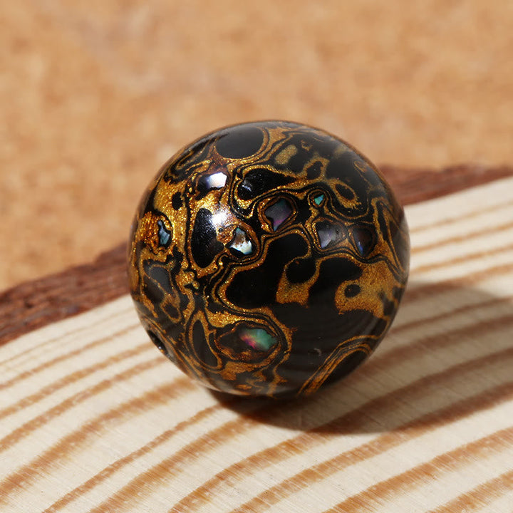 Schwarze Lackperle mit goldenem Muster auf Holzuntergrund.